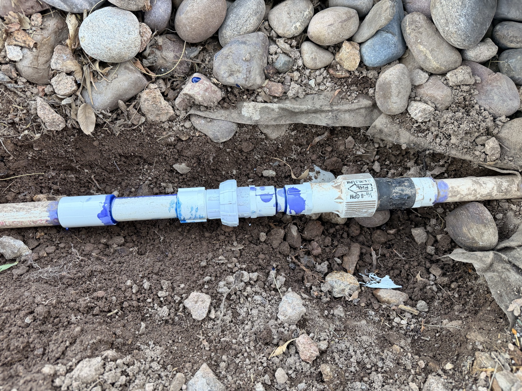 Exposed black irrigation tubing being repaired in a narrow trench
