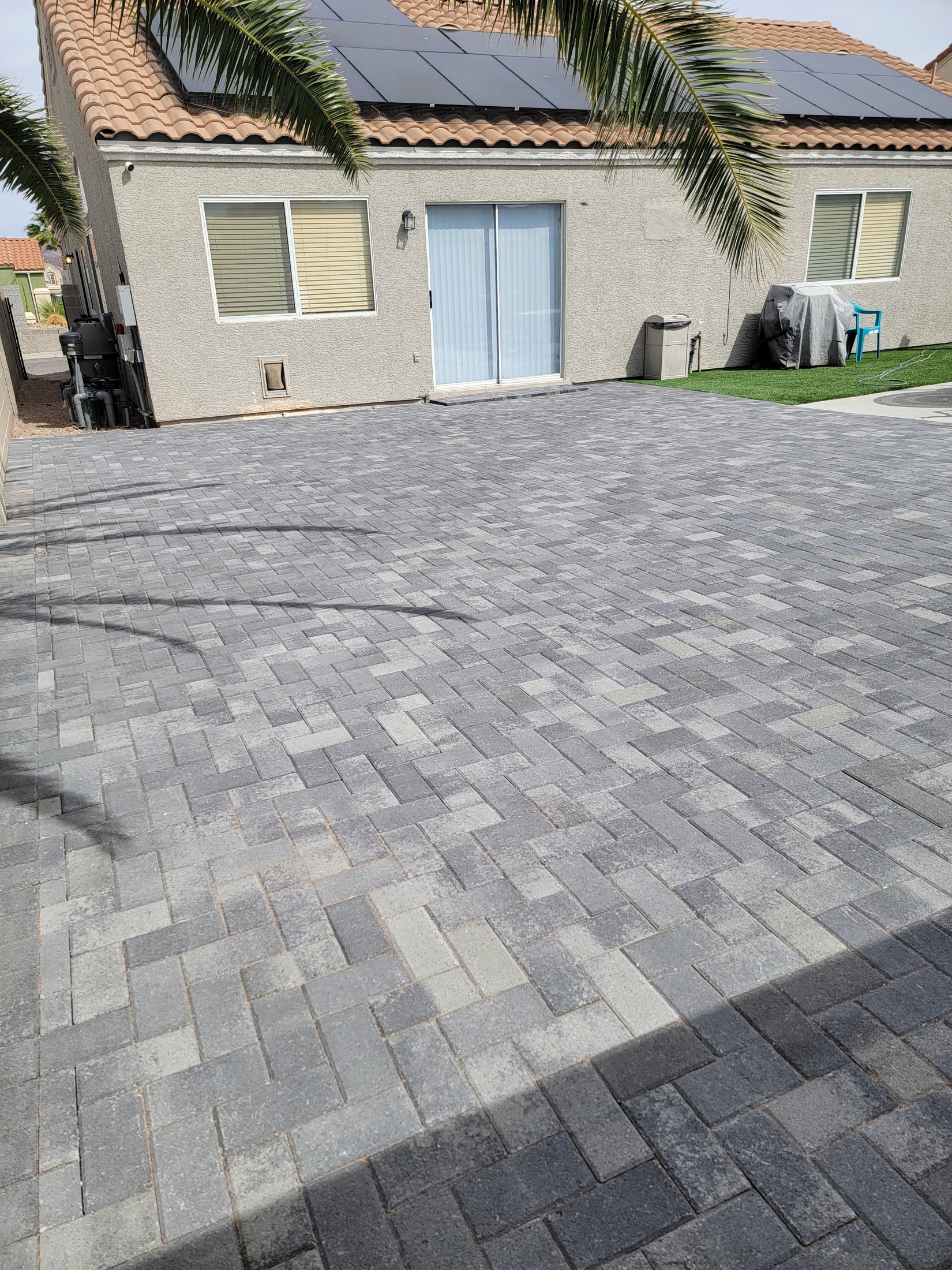Finished gray paver backyard patio beside turf and a Las Vegas home
