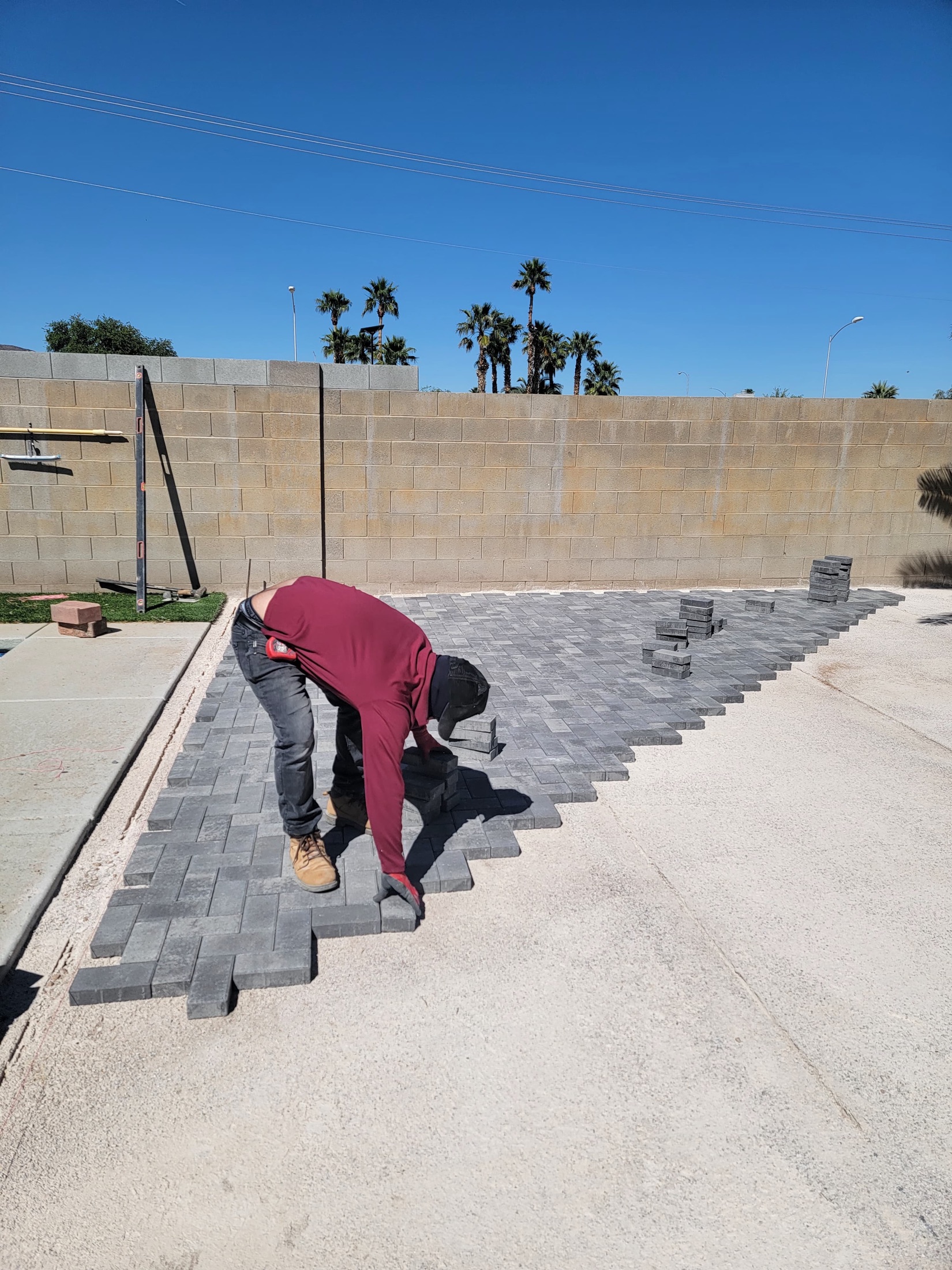 Paver installation in progress with gray pavers being placed in a backyard
