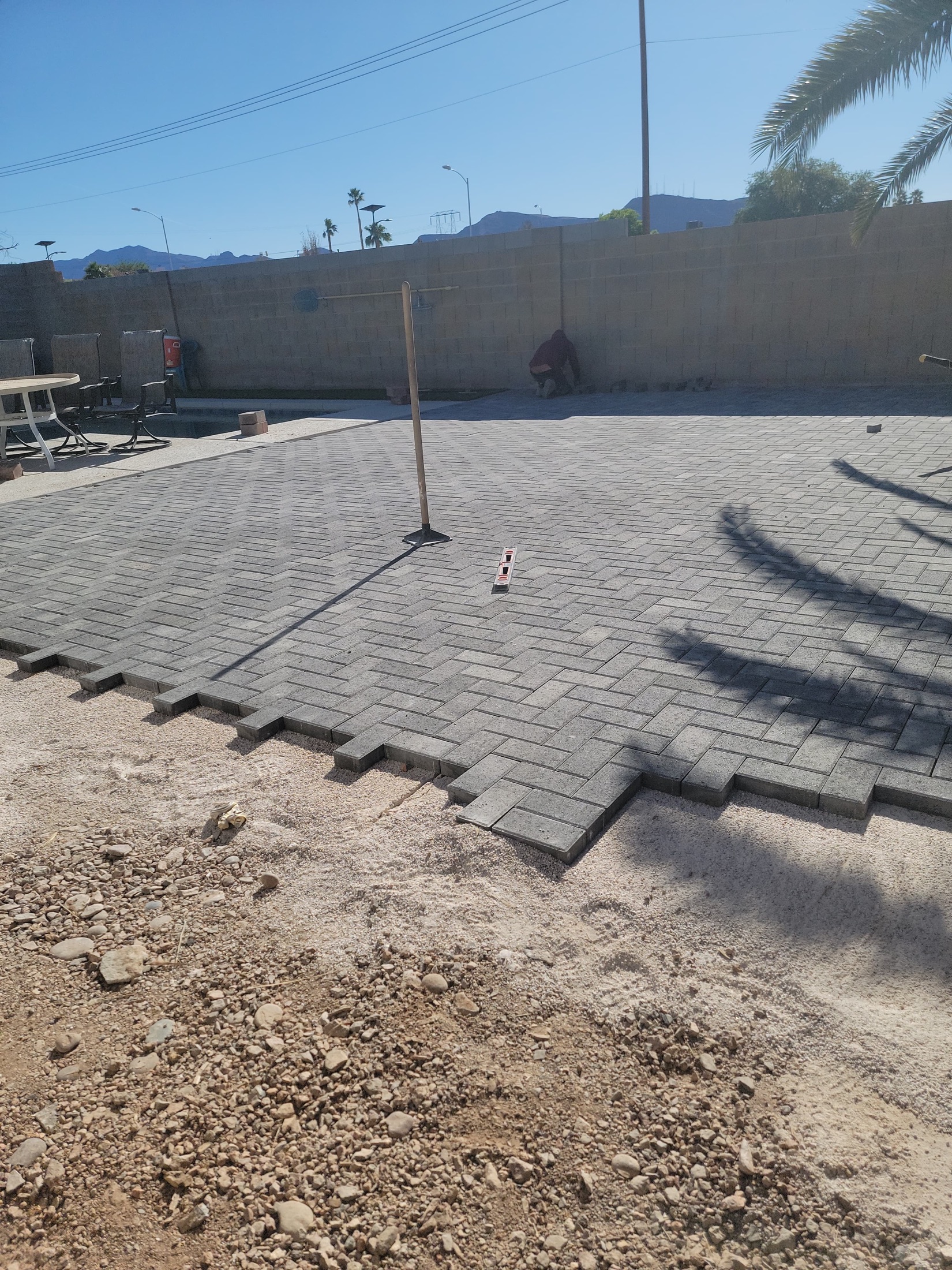 Gray paver patio layout being leveled and installed beside a pool area