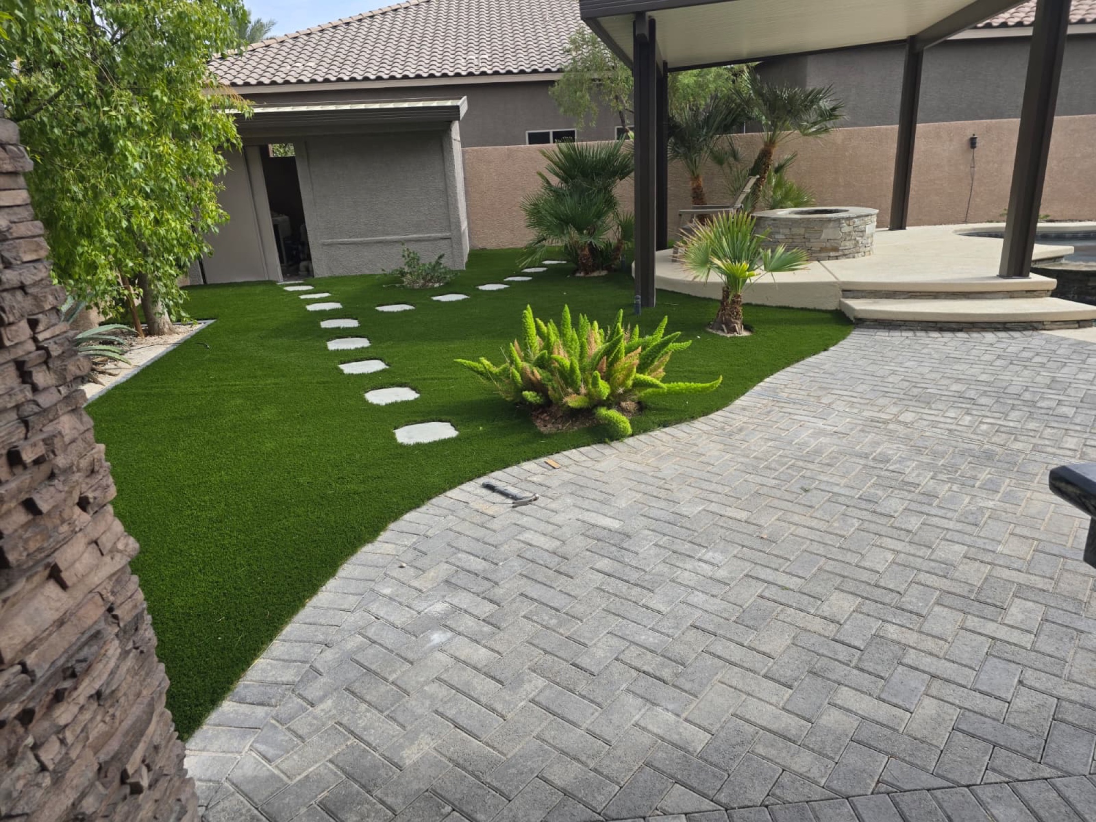 Backyard paver patio beside artificial turf, palms, steps, and outdoor living area