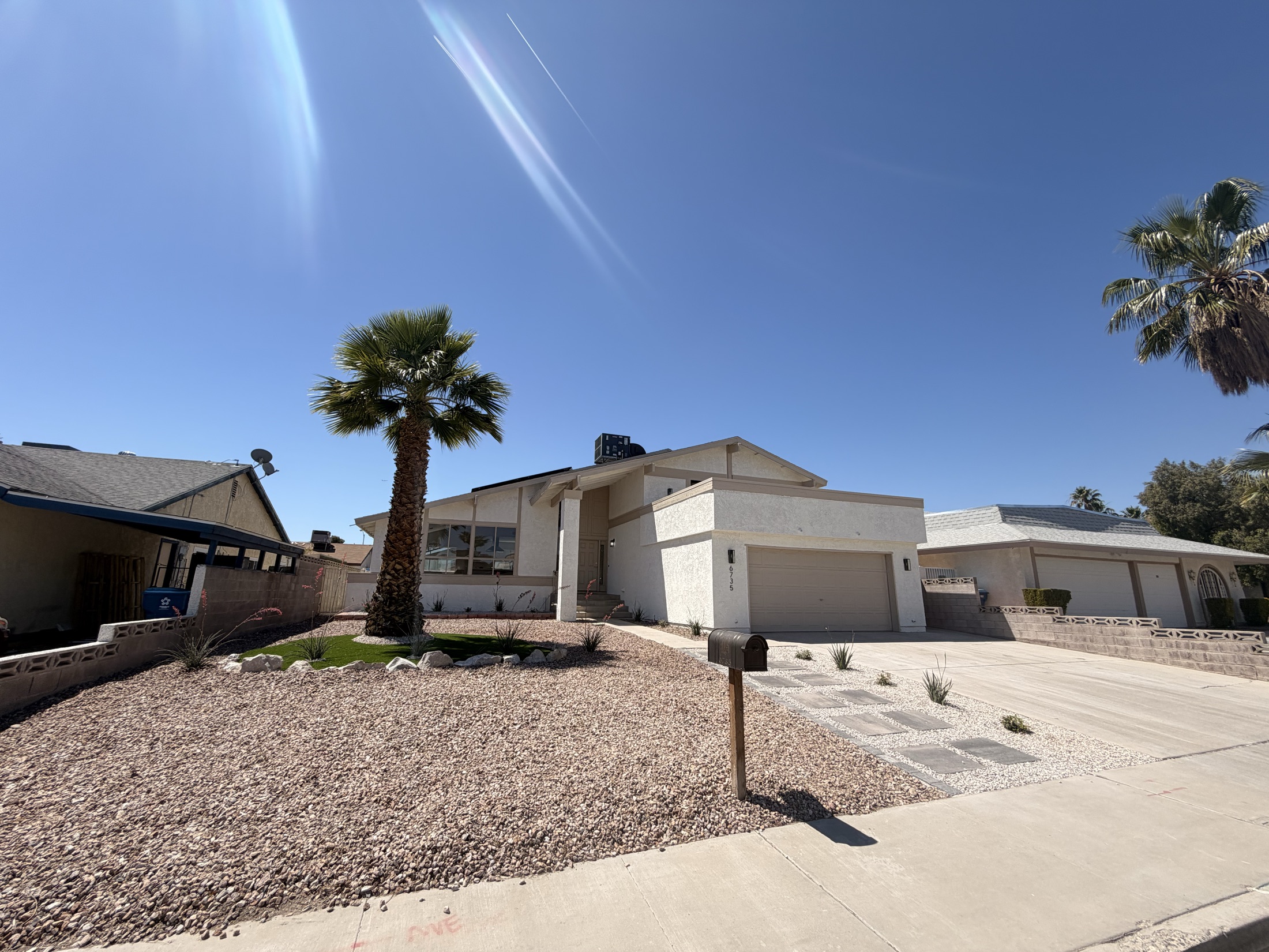Front yard desert landscape with decorative rock, palms, lighting, and planted beds