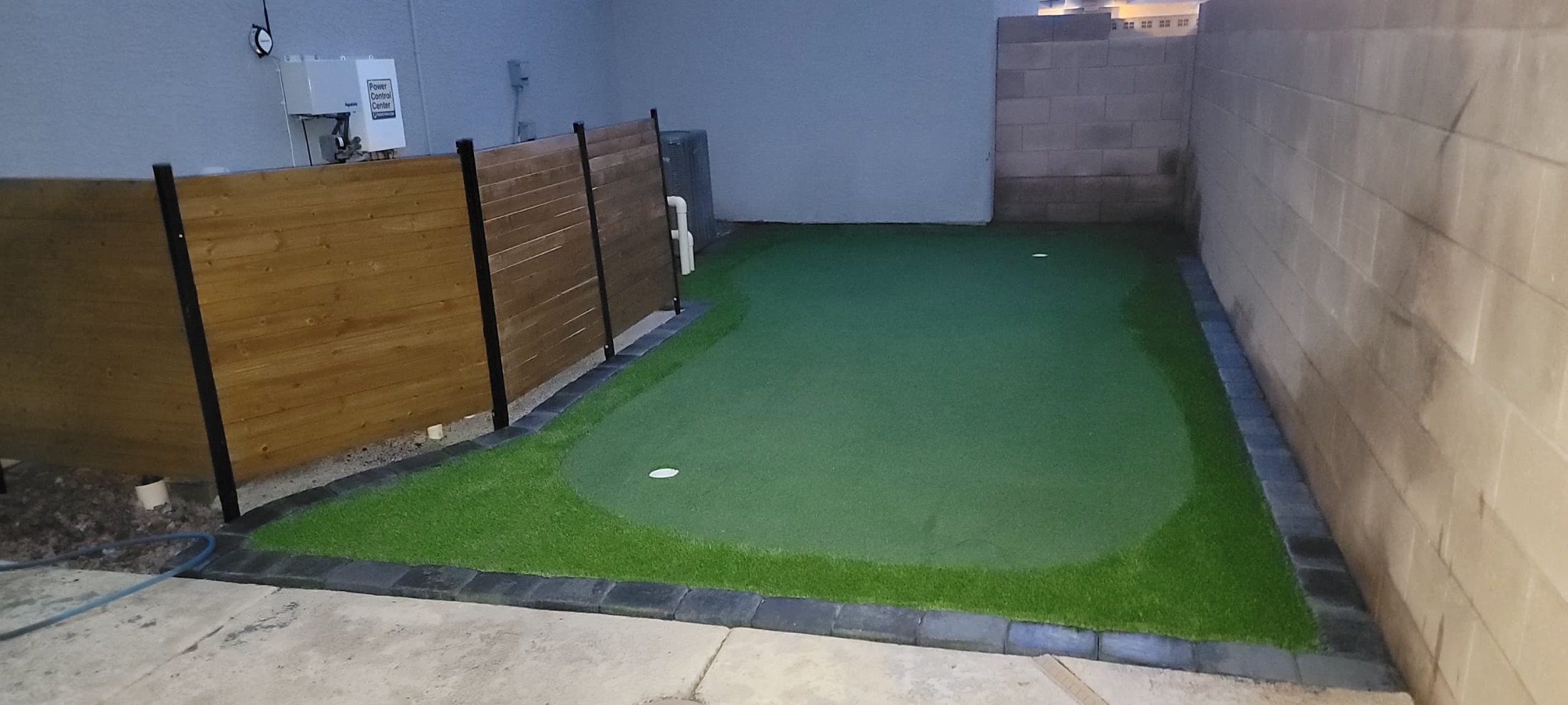 Artificial turf putting green with paver border and privacy fence