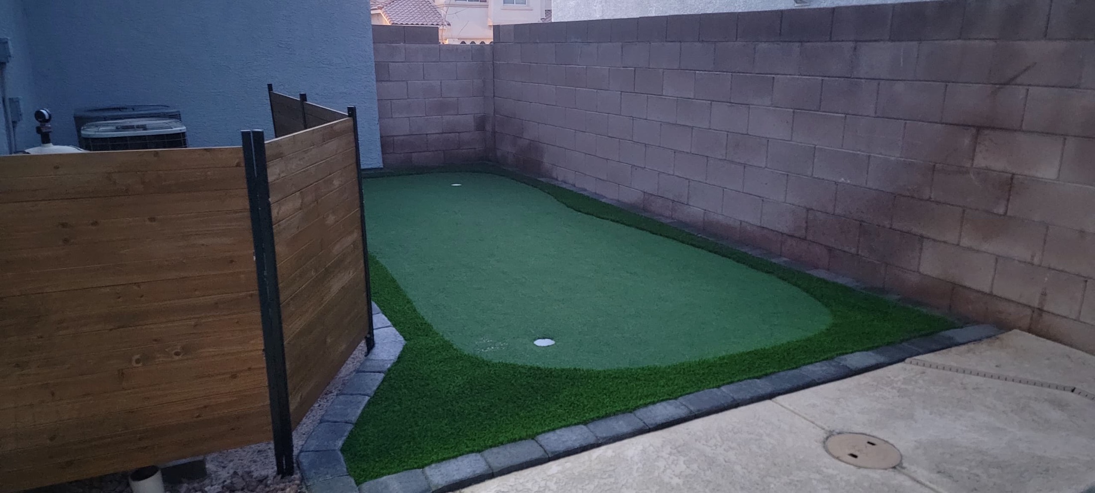 Putting green and artificial grass border beside a wood privacy fence