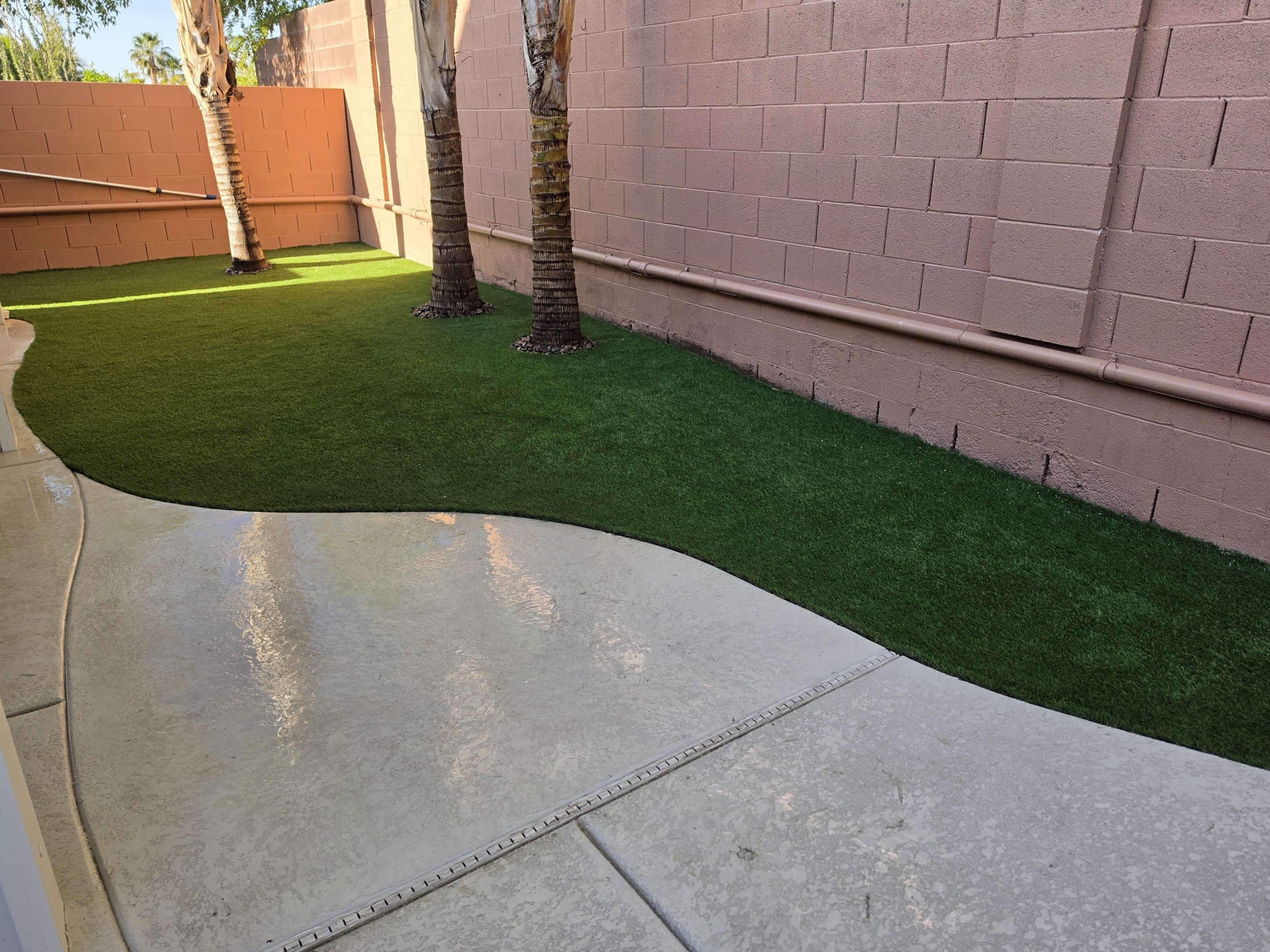 Artificial turf strip beside patio with palm trees and concrete