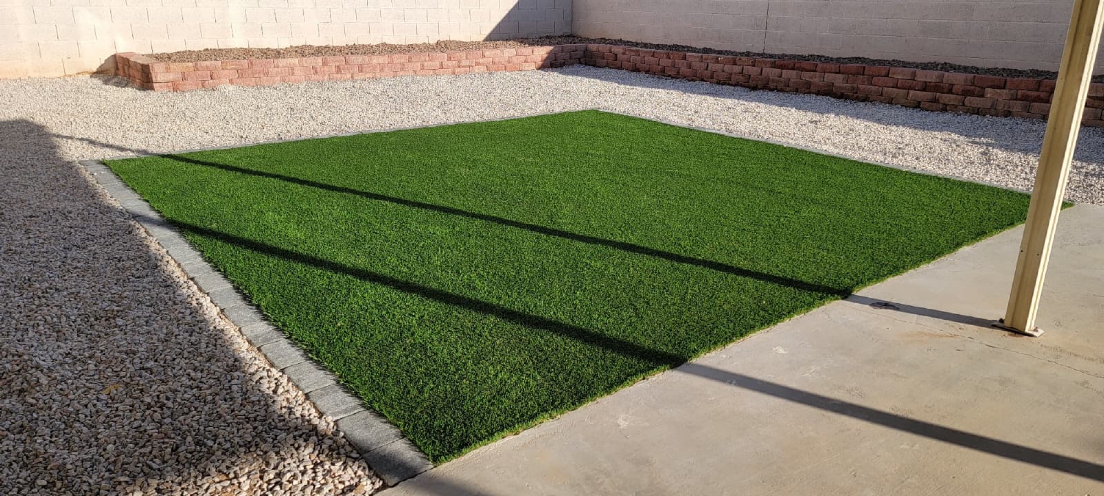 Rectangular artificial turf installation bordered by pavers and decorative rock