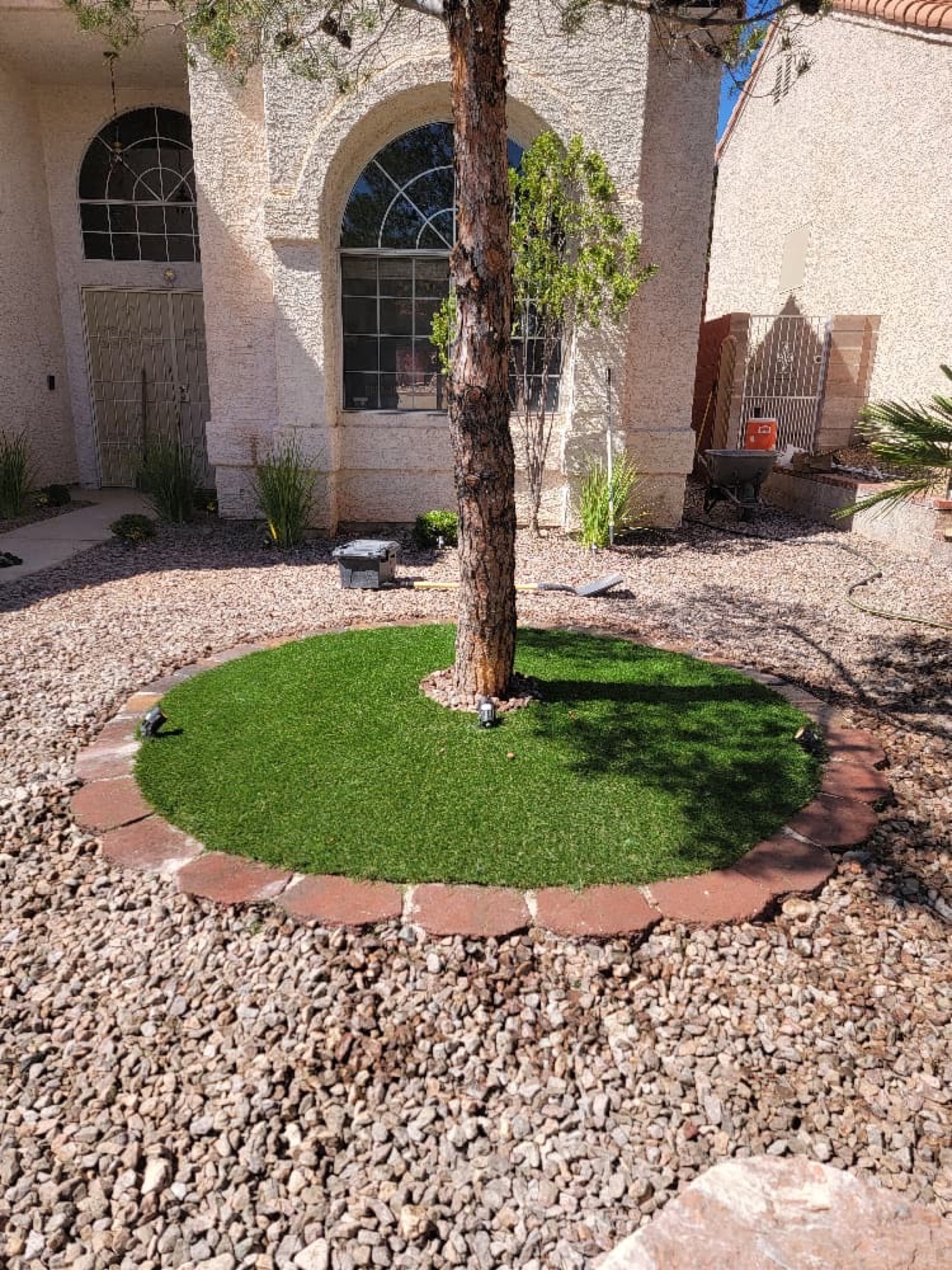 Front yard artificial turf circle around a tree with desert rock and house entry