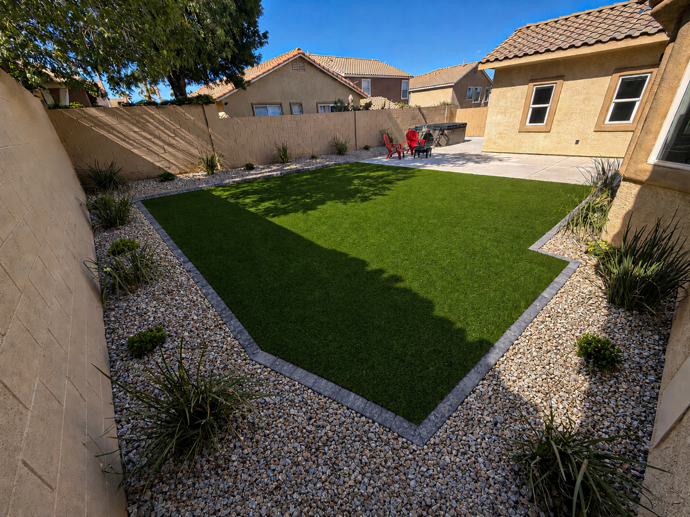 Large backyard artificial turf rectangle with rock border and desert plants