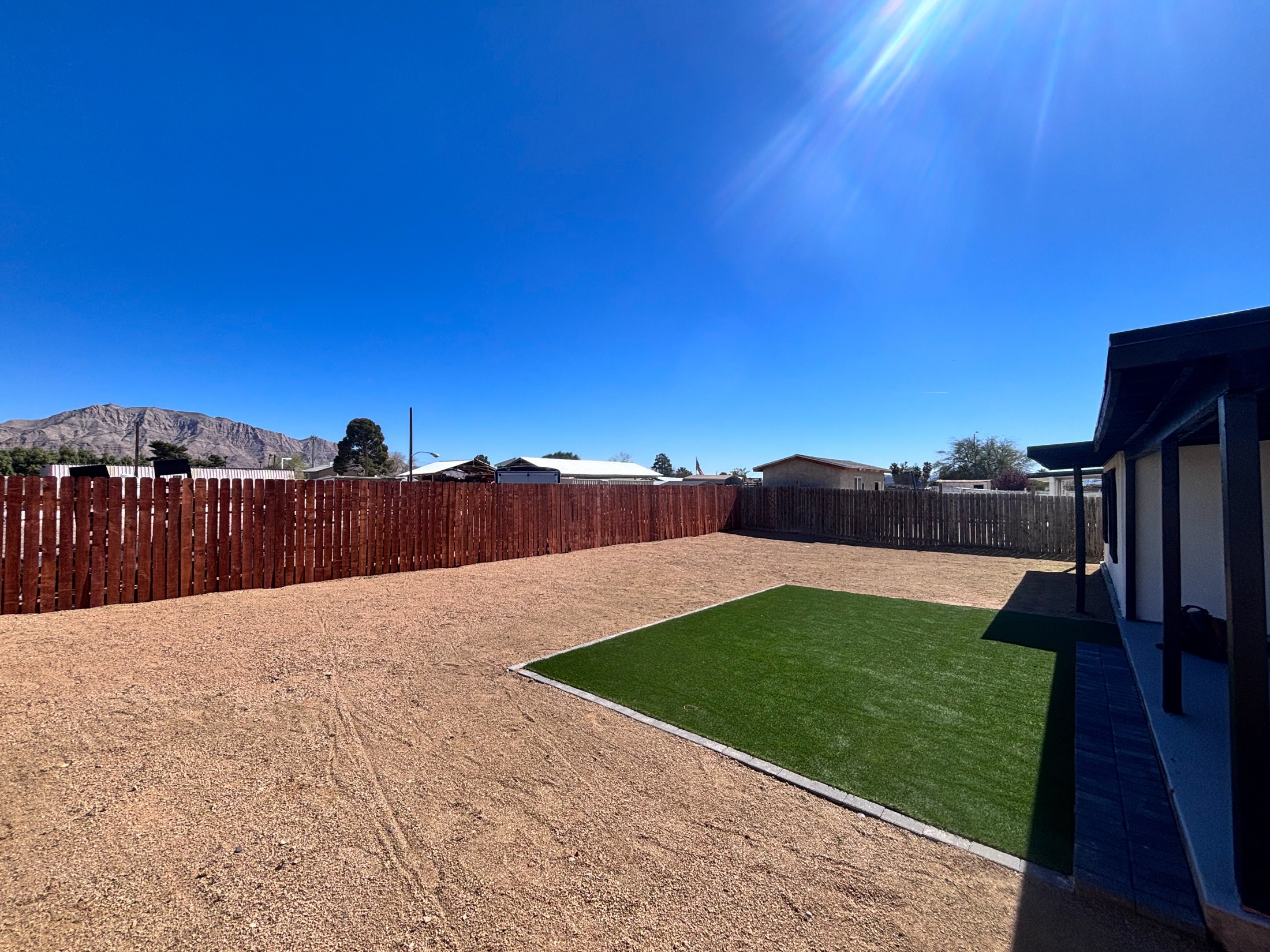 Large yard with artificial turf section, desert rock, mountain view, and wood fence